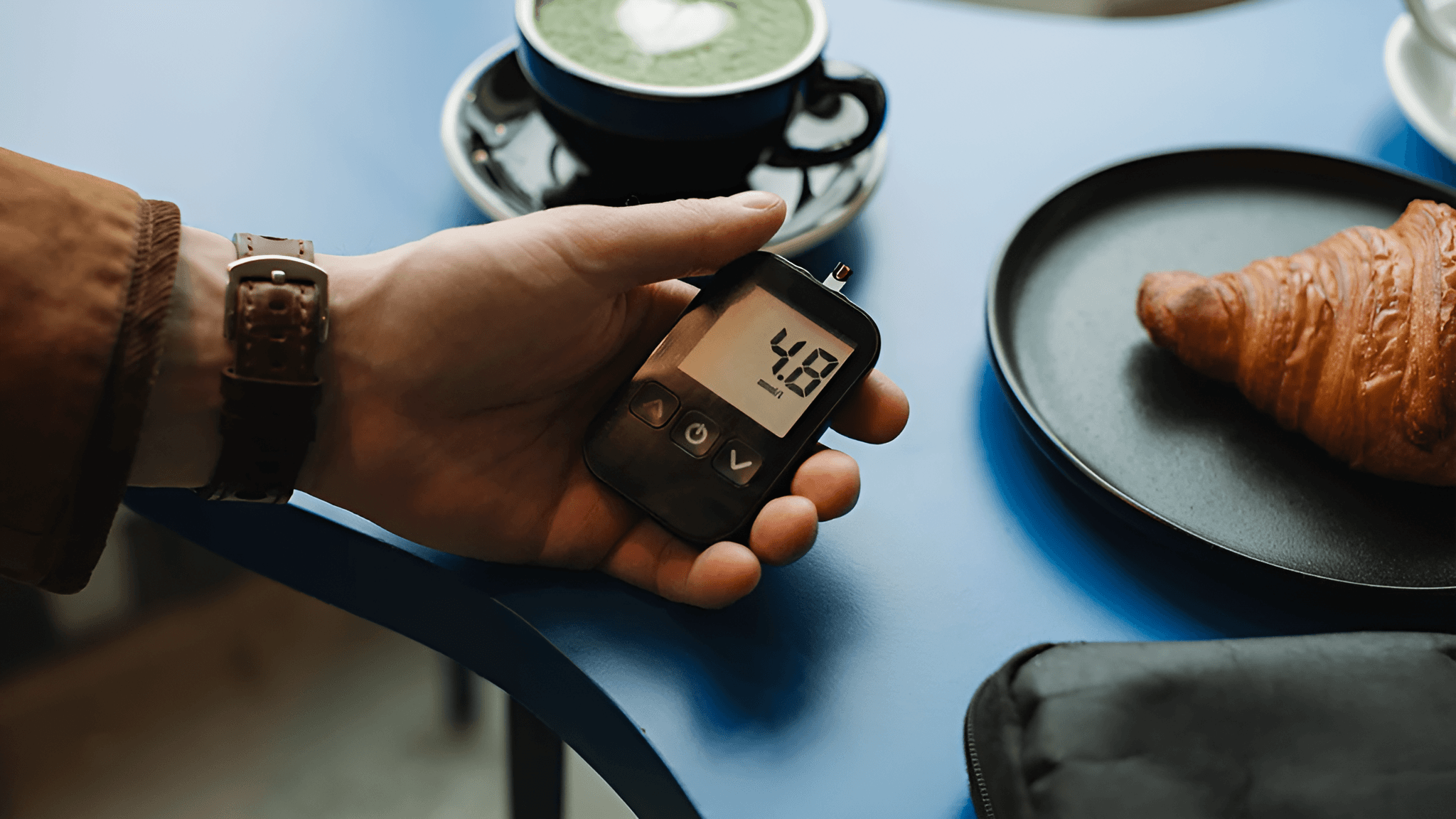 Hand holding a diabetic sugar monitor while drinking tea.